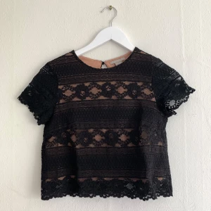 Broderad svart topp - Lite kortare topp, men skulle ej säga crop top. Passar till högmidjade jeans.  Beige under broderiet. Öppnas med knapp i nacken.