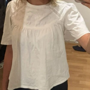 Vit blus - En vit blus med korta ärmar och rund hals. Blusen har ett detaljerat mönster på bröstet och är tillverkad i ett lätt och bekvämt material.