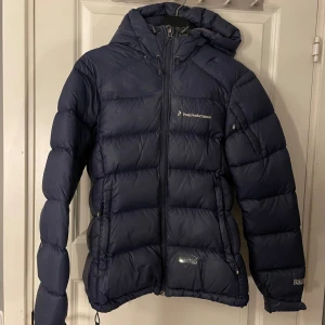 Peak Performance Dunjacka - Tjockare blå peak dunjacka i modellen frost. Ganska sliten med hål här å där vilket syns på bilderna. kan skicka mer bilder på alla hål om nån är intresserad💕