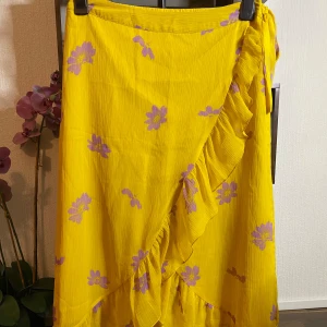 Lång somrig Kjol - Ett vanlig somrig kjol som är gul med Blom detaljer på fin material luftas när man har på sig den 