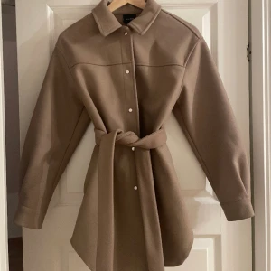 Vero moda kappa - En beige kappa från vero moda i storlek XS. Har knappar och ett knyt skärp i midjan. 