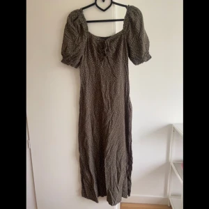 Prickig klänning - Prickig klänning i strl 38 från märket New look. Brungrön färg med puffärmar och dragkedja i sidan. Klänningen är i en midimodell. Sparsamt använd, väldigt fint skick!