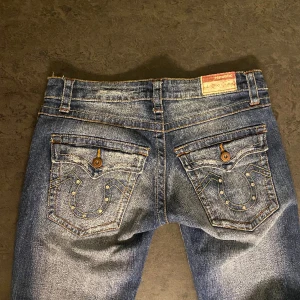Lågmidjade jeans - Supersnygga true religion- liknande jeans!! Bra skick förutom en söm som är lite uppriven (kan skicka bild i privat chatt)💕 om du vill ha fler bilder är det fritt fram att fråga!  midjemått- 78cm Innerbenslängd- 82cm