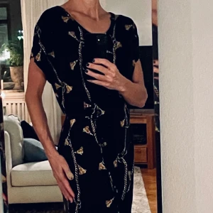 Svart klänning med guldgult mönster från Soyaconcept, stlk S - Svart knälång klänning från Soyaconcept. Guldgult mönster. Finns smalt skärp i samma tyg för mer figursydd form. Passar såväl till fest som vardag. Som ny. Stlk: S Pris: 200 SEK FRI FRAKT!