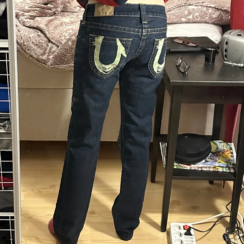 Säljer ett par jättecoola lågmidjade raka/lite baggy True Religion jeans med coola tryck på fickorna bak, storlek 28 så passar storlek S, jag har XS på bilden, jättebra skick då de knappt använda, från 2000 talet. Jeans & Byxor.
