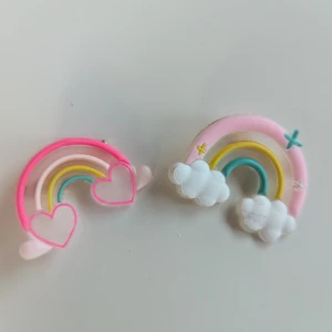 Färgglada regnbågshårklämmör med hjärtan och moln - 2st färgglada hårklämmör i form av regnbågar med hjärtan och moln. Hårklämmör har en basfärg av rosa och inkluderar färgerna gul, grön och blå. De är dekorerade med små moln och hjärtan. I fint skick  Postar inom tre dagar efter köpet