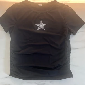 Svart t-shirt, silver stjärna på - Svart t-shirt, bra skick, silver stjärna, jätte stretchigt material, scrunch detaljer på sidorna