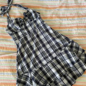 Rutig klänning från Monki - En rutig klänning i storlek S. Klänningen har ett mönster i svart, vitt, grönt och blått. Den har volangdetaljer och är ärmlös med knytband vid axlarna.