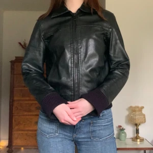 Vintage skinnjacka - Svart skinnjacka i lite bombermodell med muddar, från märket Hollies! Passar till allt ❤️‍🔥