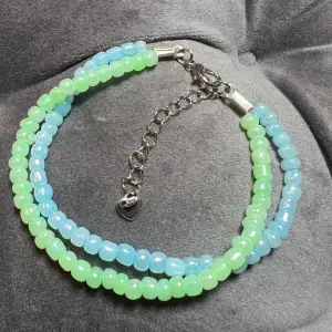Två rader med pärlor i blått och grönt med silvrigt spänne. Justerbar storlek mellan 19-24 cm.