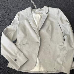 En jätte fin ljusgrå kostymjacka från H&M i strl 40. Använd endast en gång men har en liten kaffe fläck. Den är dock inte så synlig.