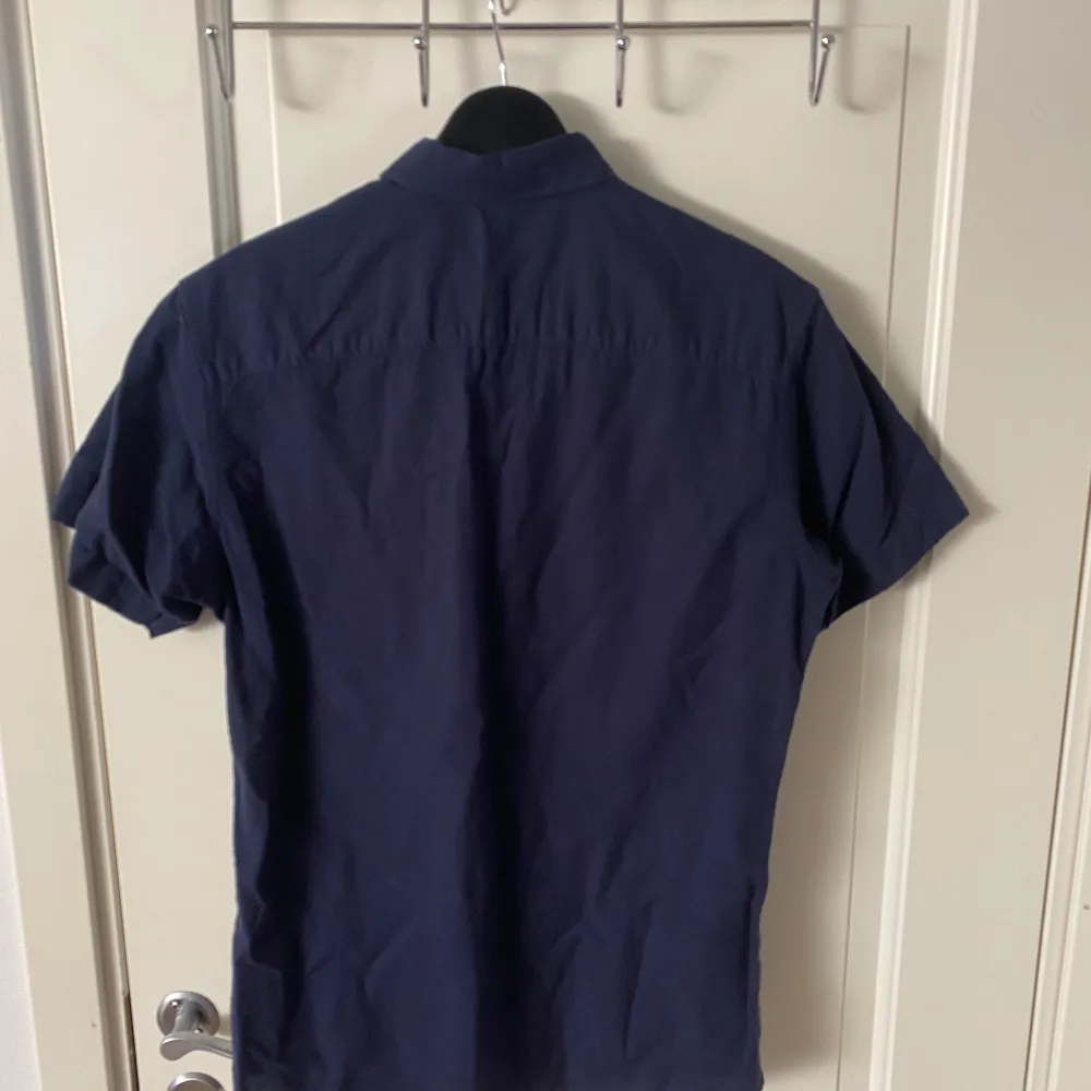 En Marinblå skjorta med korta ärmar från Jack & Jones i storleken xs. Den är använd 1-2 gånger så i super bra skick. Perfekt nu till sommaren.. Skjortor.