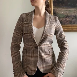 Klassisk mönstrad, figursydd Zara-kavaj i ullblandning - OTROLIGT fin och femenin kavaj från Zara. Kavajen har en knapp på framsidan och tre mindre knappar på respektive ärm, fake-fickor där fram, patches på armbågarna, samt tunnare axelvaddar som ger en timglasfigur när kavajen är på. Storlek S.