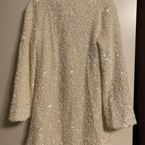 Vit paljettklänning H&M  - En kort A-linjeskuren klänning i mjuk velour klädd i skimrande paljetter. Trikåfodrad.  Denna klänning blev viral och såldes snabbt ut! Säljes i mycket fint skick!  