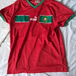 Marocko fotbollströja - Skick 8/10. Säljer den för att den inte passar och för att den inte används. Det är marockos vm tröja 2022. Skriv vid minsta fråga eller fundering.