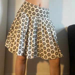 Utsvängd mönstrad kjol - Cool och trendig kjol i vitt med mönster av bruna blommor/klöver. Står storlek 34 men passar mig som brukar ha s och är 165 cm. Dragkedja på sidan. Kan mötas på söder eller posta. Skriv helst innan ni trycker köp nu då jag är borta en del i sommar. 