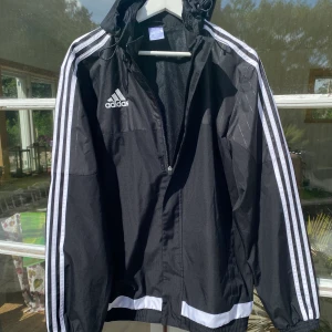 Adidas Regnjacka svart/vit - Hej, säljer en oanvänd Regnjacka från Adidas i svart med vita detaljer. Utmärkt skick. Storlek M, passar även L. Köptes för 900kr. Pris kan alltid diskuteras. Hör av dig vid intresse! 