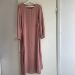 Klänning  - Axlarna är 36 cm, längden är 135 cm , ärmlängd är 63,5 cm och byst är 100 cm. Färgen är ljus rosa. Den passar i sommaren. 