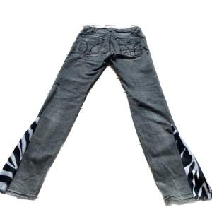 Jättesnygga gråa jeans med dragkedje-detaljer och zebra-bootcut. Knappen på framsidan sitter lite löst men sitter fast, därav lite lägre pris. Midja 37cm. Innerben 76cm.