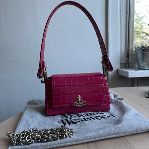 Vivienne Westwood väska - Liten rosa Vivienne Westwood ”Hazel” väska i väldigt bra skick. Köpt från VW’s hemsida, använd ett par gånger enbart.  Mått 17cm bred x 10cm hög. Medföljer originell dustbag och kedja till väskan. 