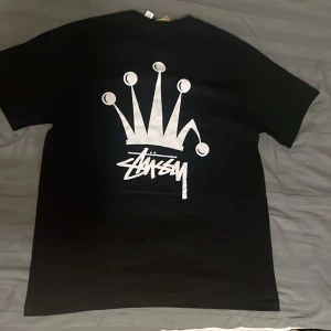 Stussy Crown Black T-shirt - Stussy Tee Crown med svart bas. Kondition är helt ny då baggy fit-en inte var som jag gillade. Alla tags sitter kvar och plastpåse inkluderar! Kontakta vid vidare frågor 👍  OBS⚠️⚠️ kommer ta bort anonsen efter 19/05, Sålänge ingen köper plagget!