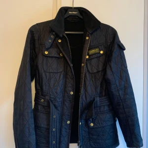 Babour svart quiltad jacka  - Svart, fodrad quiltjacka från Babour. Skärp i midjan. Bra använt skick. Stl 38. 