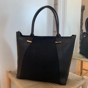 Handväska med gulddetaljer  - Säljer denna snygga handväska från Kappahl. Mått: H30, L35, B18 cm. Köpte den för ca 6 år sedan men har bara används ett fåtal gånger. Så den är i nyskick. Inköpt för 399kr. Hör av dig vid frågor💗