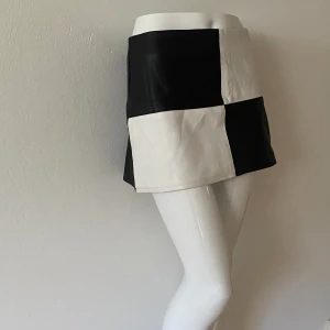 Kjol - Vintage tvåfärgad mini kjol i läderliknande material, midjan är 37 cm och längden är 31 cm. Perfekt skick förutom att biten man drar i på blixtlåset har gått av, syns på bild!