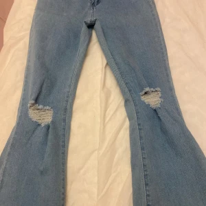 Blåa utsvängda jeans - Utsvängda jeans med splitt och hål på knät. Små i storleken 