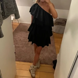 Klänning  - Volangklänning med en arm. Svart klänning med volanger och en arm. Perfekt till fest. Storlek Xs men passar även S 