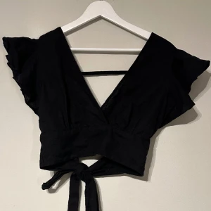 Bikbok blus  - En svart Linné blus från Bikbok i storlek S. Toppen är croppad, djupt v-ringad och har volanger vid axlarna. Den är öppen i ryggen och har band för att knyta en rosett. 
