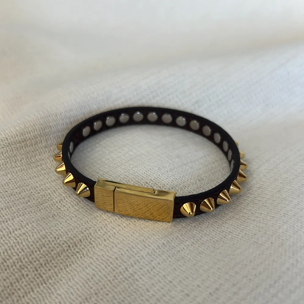 Armband från Edblad i brunt läder med nitar i blank 14K guldplätering på rostfritt stål (nickelsäkert). Köpt för 499 kr och i nyskick förutom att en av nitarna har ramlat av (se bild 4) och några knappt märkbara/ pyttesmå repor på magnet låset.. Accessoarer.