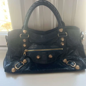 Balenciaga väska - Säljer en jätte fin Balenciaga väska i marinblå med guldiga detaljer. Köpte dyrt på plick men tyvärr finns det inget äktabevis! Kom med frågor! Finns ändas dessa bilder. Väskan kommet också med ett längre axelband! Måtten är 25 x 9,5 x 38(cm)💕💕💕💕