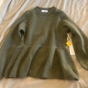 Stickad tröja  - En mörkgrön stickad tröja som svänger ut lite där nere och har ballong armar, oanvänd.