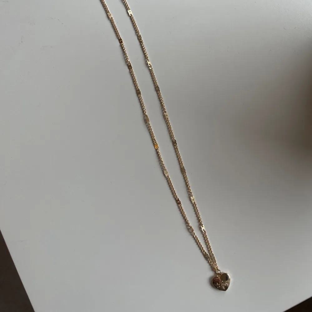 Halsband i rostfritt stål med guldplätering, ett hjärta där det står love, aldrig använt . Accessoarer.