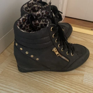 Sneakers med inbyggd klack - Super snygga svarta sneakers med inbyggd platåklack.💞 Det är guld detaljer på skorna och leopardmönster på insidan. Framsidan är även lite glittrig. 4/5 i skick, inga skador bara att de är lite använda