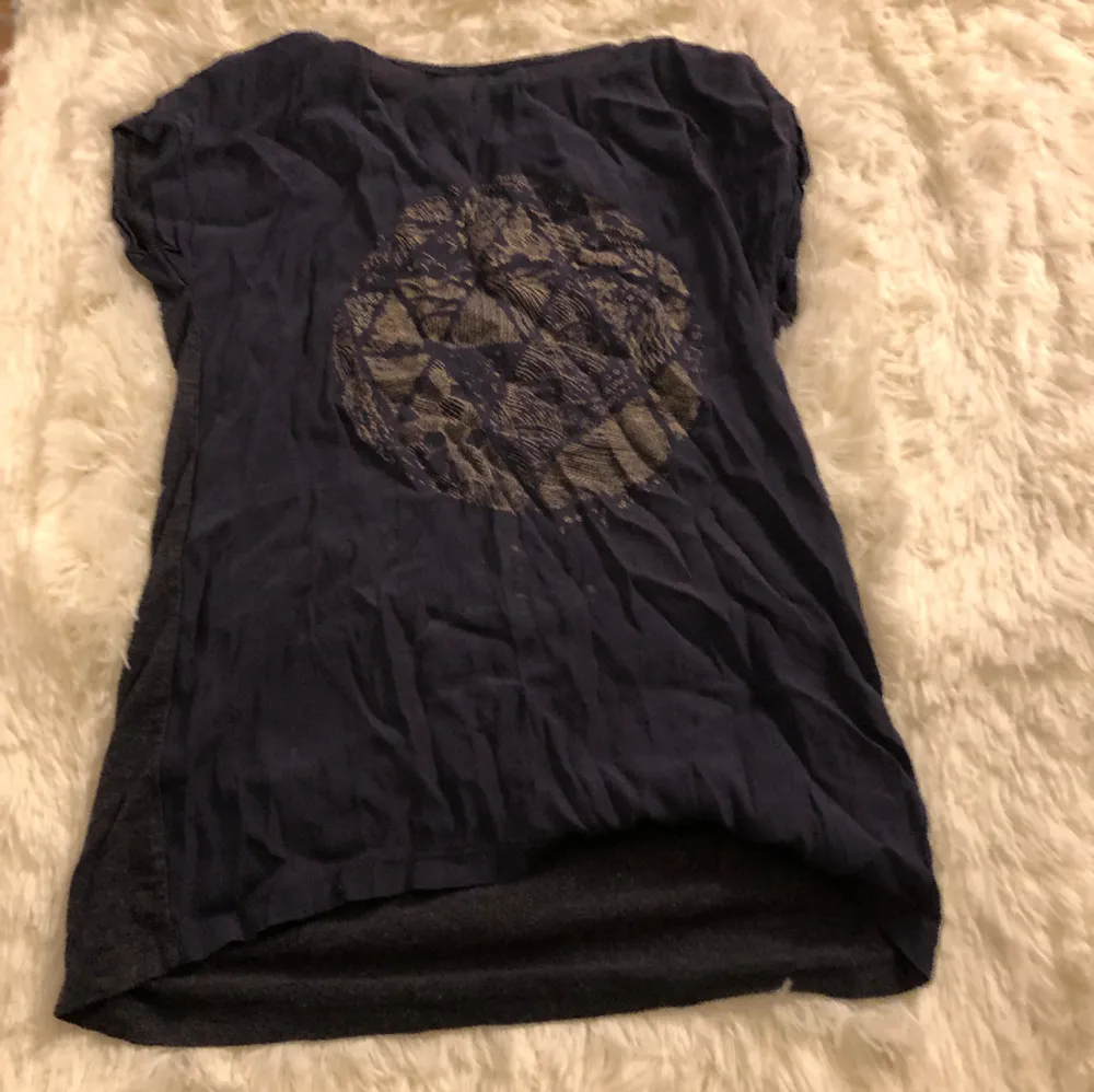 En mörk blå T-shirt med en cirkel där fram med en massa mönster i och ett litet hål vid nacken men det ska vara där. T-shirts.