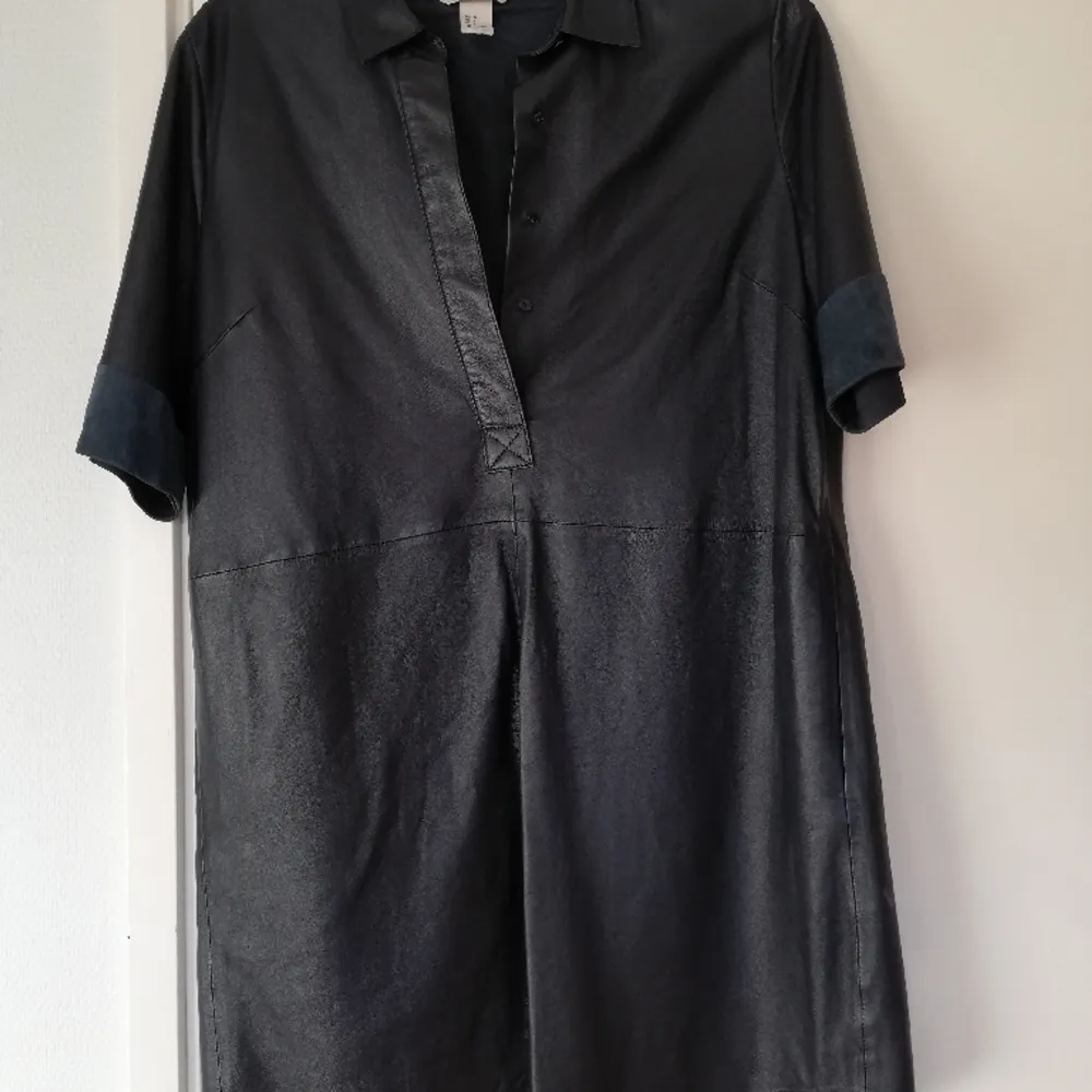 En svartblå lång kortärmad skinnskjorta från HM som kan funka som kort klänning. I mycket bra skick. I en mörkt blå färg som nästan kan uppfattas som svart. . Skjortor.