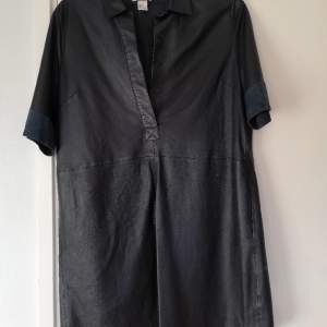 En svartblå lång kortärmad skinnskjorta från HM som kan funka som kort klänning. I mycket bra skick. I en mörkt blå färg som nästan kan uppfattas som svart. 