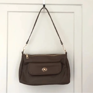 Söt brun väsla - En söt brun väska som är köpt här på plick som tyvärr aldrig blivit använd. Väskan är mellanstor och har ett fack på framsidan. 