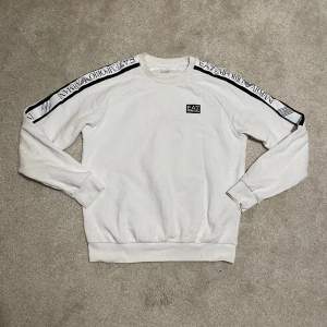 EA7 Emporio Armani vit sweatshirt, storlek Small. Snygg märkessweater. Ord. pris 1249 kr – ett exklusivt erbjudande på denna stilfulla och bekväma sweatshirt!