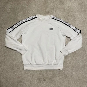 EA7 Emporio Armani Vit Sweatshirt - Exklusiv Stil till Ett Förmånligt Pris! - EA7 Emporio Armani vit sweatshirt, storlek Small. Snygg märkessweater. Ord. pris 1249 kr – ett exklusivt erbjudande på denna stilfulla och bekväma sweatshirt!