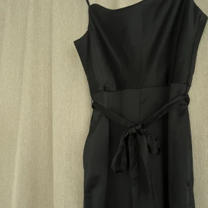 Svart jumpsuit i satin - Jumpsuit som endast kommit till användning vid ett tillfälle, lyxig känsla med långa ben och knyte i midjan   Passar 34/36