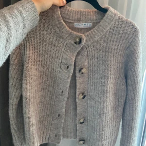 Kofta - Grå beige varm kofta i stickat material. Köpt på primark men har inte kommit till användning. Jättefin att knäppa första knappen eller hela vägen!