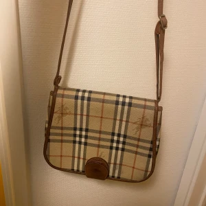 Burberry väska  - Hej säljer denna väldigt fina Vintage Burberry väska köpt i en designer vintage i Paris.  Äkta läder.  Små slitningar men inget större  Väldigt snygg på sommaren. Både till herr och dam. Är själv kille och använt den till snygga outfits.   