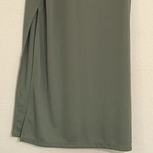 Grön klänning från H&M - En elegant grön klänning från H&M med smala axelband och en slits på sidan. Klänningen har en enkel och stilren design, perfekt för olika tillfällen.