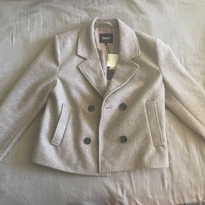 Grå kort kappa  - Grå/beige kappa från only i storlek S. Den är oanvänd med prislapp kvar. Nypris 749kr 