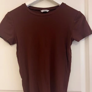 Brun t-shirt från Estelle - En enkel och stilren brun t-shirt. T-shirten har korta ärmar och en rund halsringning.