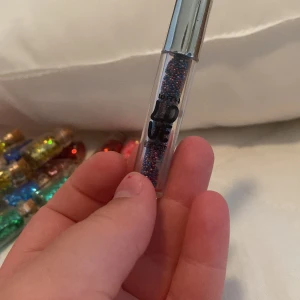 Glittrig läppglans - Ett glittrigt läppglans i en genomskinlig tub med silverlock. Läppglanset innehåller flerfärgat glitter och ger en skimrande effekt på läpparna.