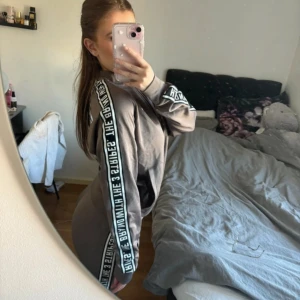 Grå hoodie från Adidas - hoodie och byxor från Adidas med textdetaljer längs ärmarna. Tröjan har en dragkedja framtill. 